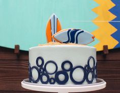 a white and blue cake sitting on top of a table next to a surfboard