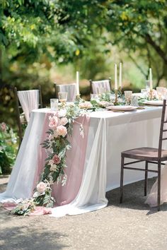 the table is set with white linens, pink flowers and greenery on it