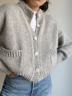 a woman is wearing a gray cardigan sweater and blue jeans with her hands on her hips