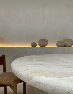 a table and two chairs in a room with white marble walls, lighting above the table