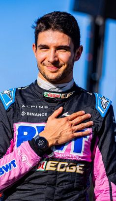 a man with his arms crossed standing in front of a tall building wearing a pink and black outfit