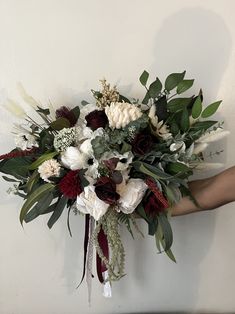 a bouquet of white and red flowers is held by someone's hand against a wall