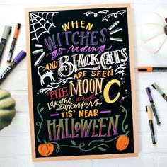 a halloween chalkboard with witches and black cats written on it next to markers, crayons, and pumpkins