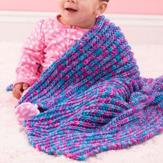 a baby is sitting on the floor with a knitted blanket in pink and blue