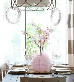 a dining room table set for two with flowers in a vase on the centerpiece