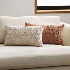 two decorative pillows sit on the back of a couch in front of a framed mirror