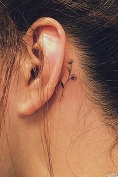 a woman's ear has a small flower tattoo on it