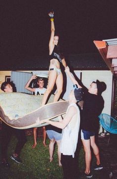 a group of people standing around a woman on top of a skateboard in the grass