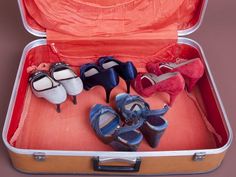 four pairs of shoes are in an open suitcase with the lid down and one pair is wearing high heels