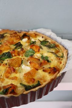 a quiche with spinach, cheese and other toppings in a paper container