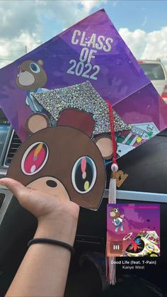 someone is holding up a graduation cap with a bear face on it and other decorations in the background