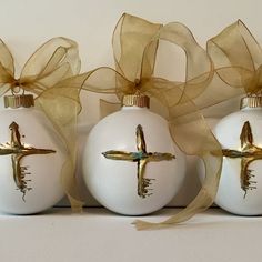 three white christmas ornaments with gold accents and a cross on the front one has a brown ribbon