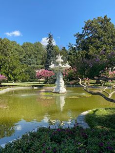 a fountain surrounded by flowers and trees in a park