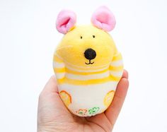 a hand holding a yellow stuffed animal with pink ears