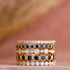 three stacking rings with black and white stones on top of each other in front of a pink background