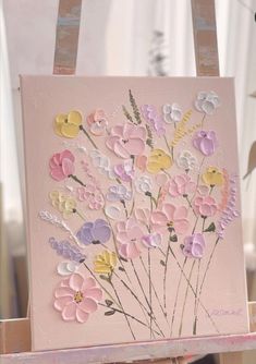 an easel with a painting on it and flowers painted on the canvas in pastel colors