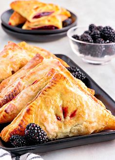 blackberry turnovers and blackberries on a plate with two bowls of berries in the background