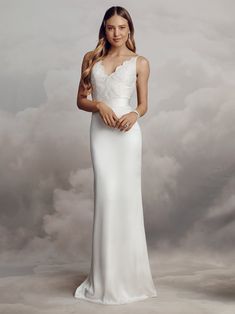 a woman in a white wedding dress posing for the camera with clouds behind her and she is looking at the camera