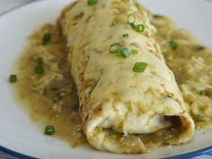 an enchilada on a white plate with green onions and gravy