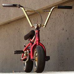 a red bike parked next to a concrete wall with no one on it's seat