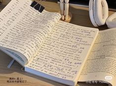 an open book sitting on top of a desk next to headphones and a pen