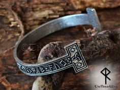 a metal bracelet with an ornate cross on it, sitting on top of a piece of wood