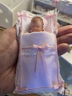 a hand holding a tiny baby doll in a pink blanket with lace trims on it