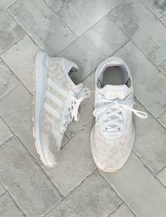 a pair of white adidas sneakers sitting on top of a tile floor