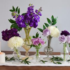 a table topped with vases filled with purple and white flowers next to a candle