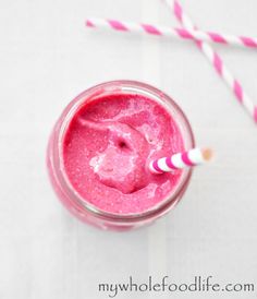 a pink smoothie in a glass with two straws next to it on a white surface