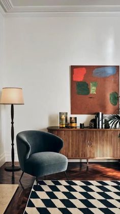 a living room with a black and white checkerboard rug, blue chair and painting on the wall