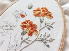 an embroidered flower is shown on a piece of white fabric with orange and yellow flowers