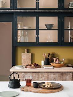 a kitchen counter with plates and cups on it next to a wooden board that has glass doors