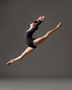 a woman in black leotard and ballet shoes is doing a split leg pose