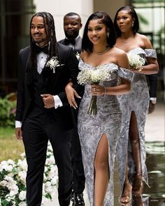 a man and woman in formal wear walking down the aisle with other people behind them