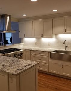 a kitchen with white cabinets and marble counter tops