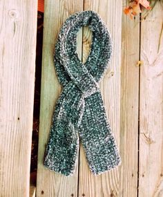 a green and white scarf sitting on top of a wooden fence next to an orange flower