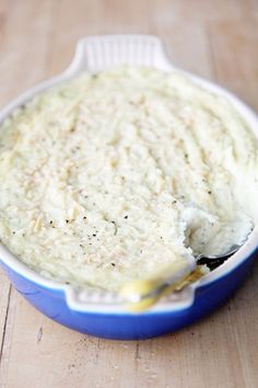 a blue dish filled with mashed potatoes on top of a wooden table