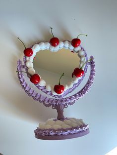 a small mirror with cherries on it sitting on top of a table in front of a white wall