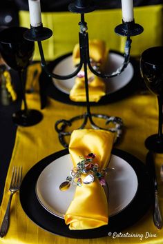 the table is set with yellow napkins and black place mats, silverware, and candles