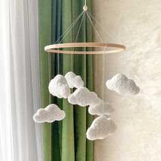 a white crocheted cloud mobile hanging from a curtain in front of a window