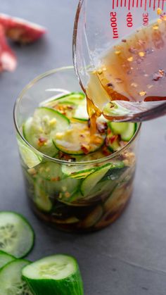 a person pouring dressing into a glass bowl filled with cucumbers