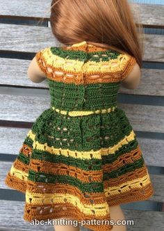 a crocheted doll wearing a green and yellow dress on top of a wooden bench