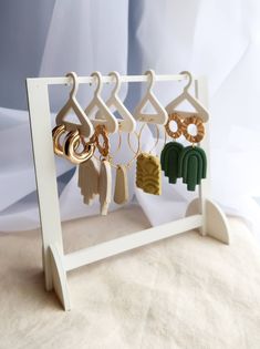 several pairs of earrings hanging from hooks on a white rack with beige and green tassels