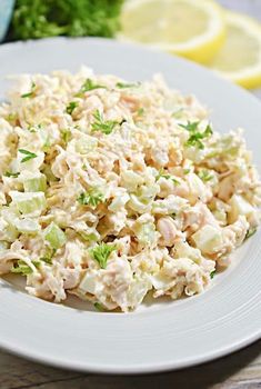 a white plate topped with chicken salad next to lemon wedges