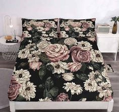 a bed covered in black and pink flowers on top of a wooden floor next to a night stand