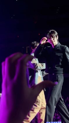 a man standing on top of a stage in front of a purple light with his hand up