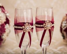 two wine glasses with red ribbon and jeweled decorations on the rims are sitting next to each other