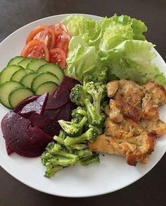 a white plate topped with meat and veggies next to sliced cucumbers