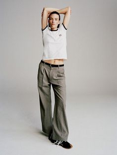 a woman in white shirt and grey pants posing for a photo with her hands behind her head